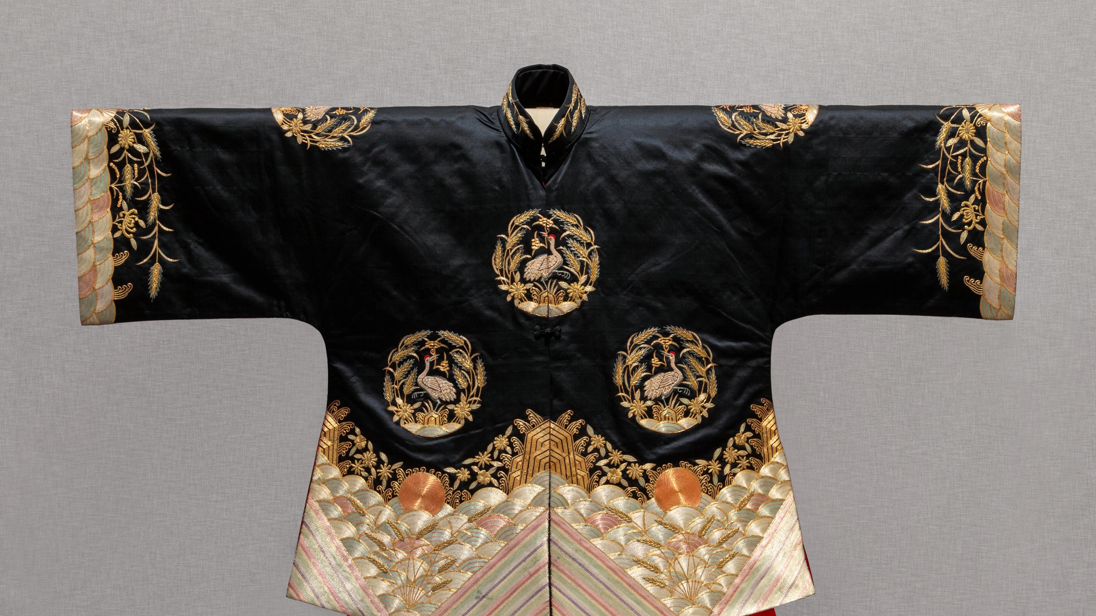 A traditional black robe features intricate gold embroidery with circular dragon motifs. 