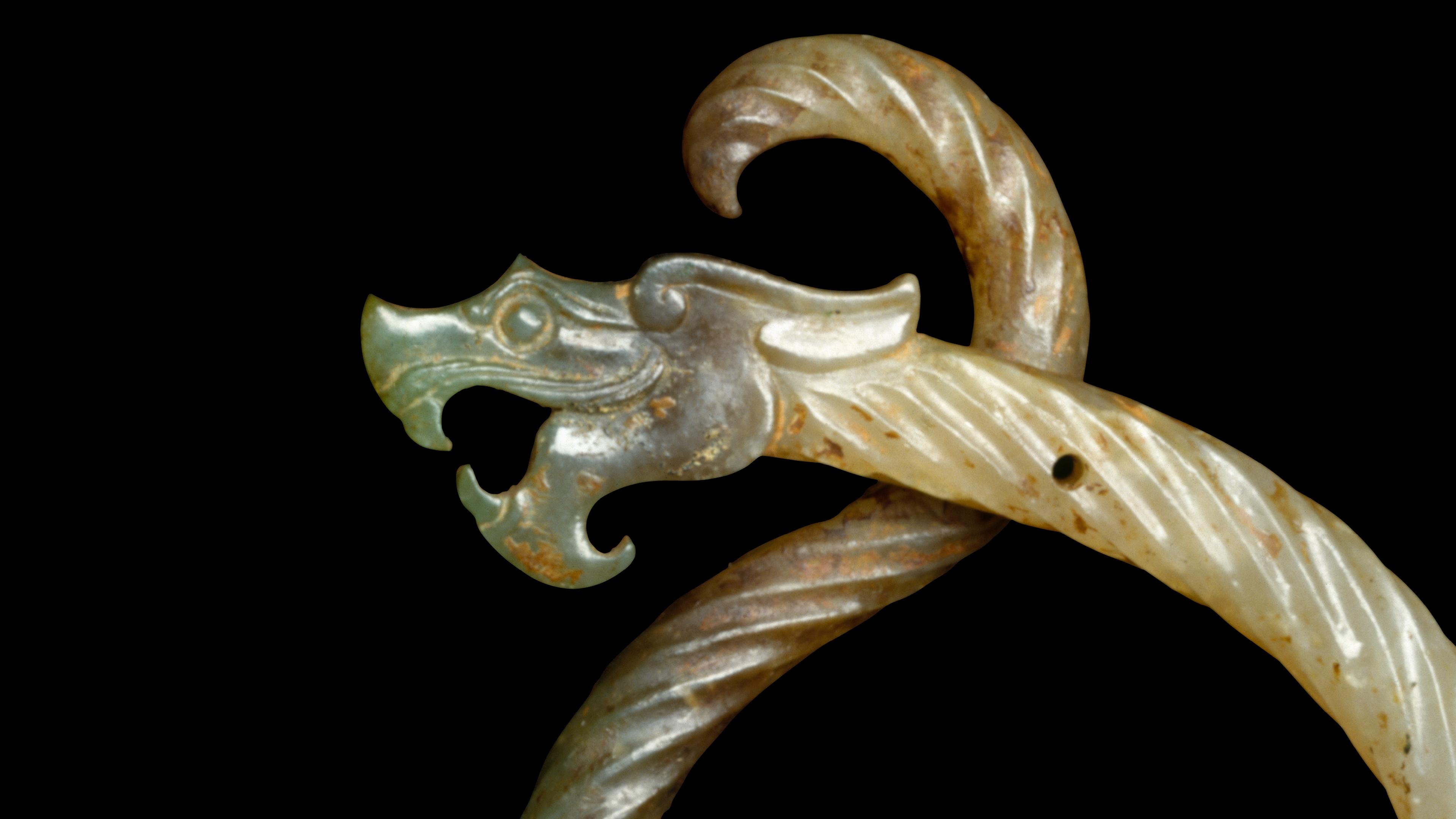 A carved jade ornament featuring a dragon's head with an open mouth and spiral body against a black background.